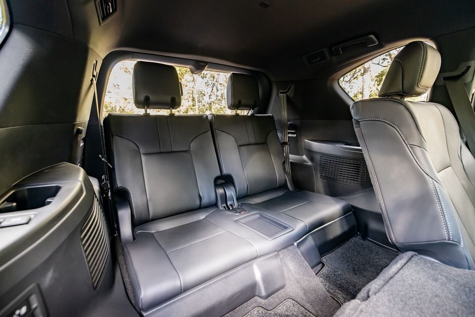 Interior rear seating of a 2026 Lexus LX700h Sports Luxury SUV showing three dark leather seats with a central armrest and rear climate vents