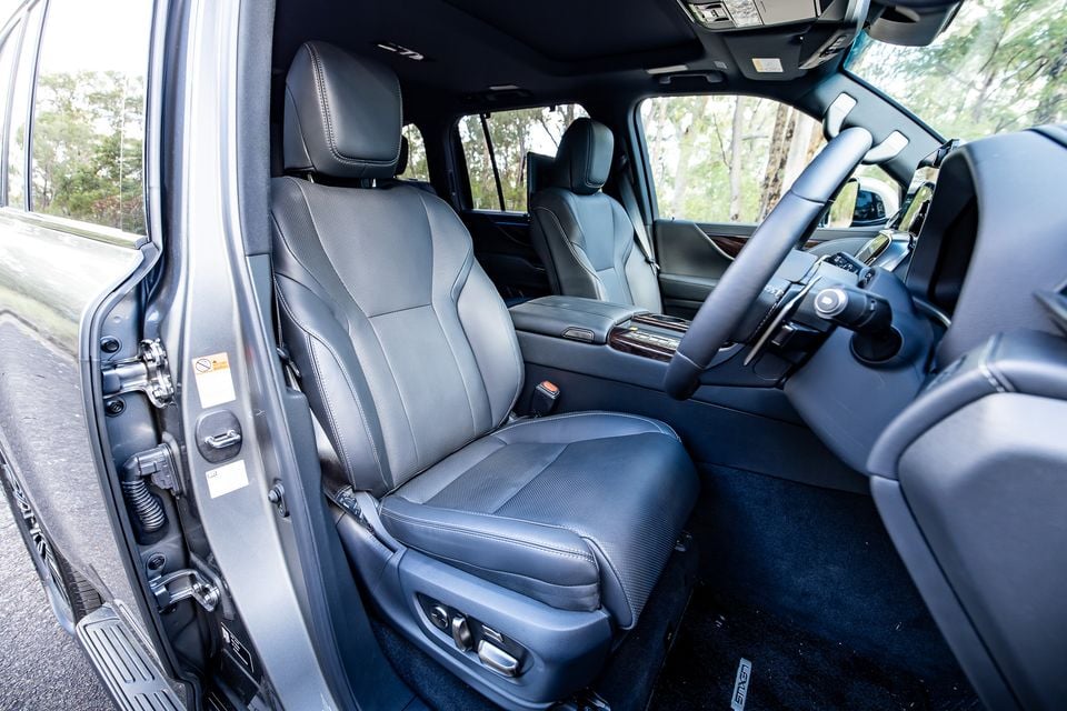 Interior view of a 2026 Lexus LX700h Sports Luxury showing the front seats with dark leather upholstery, centre console with timber trim, and steering wheel