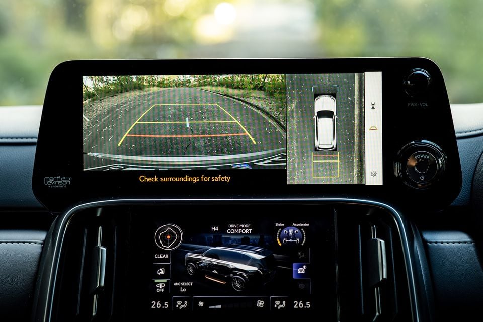 The dual infotainment screens of a 2026 Lexus LX700h Sports Luxury showing the reversing camera with overhead surround-view display on the upper screen, and the vehicle dynamics and drive mode settings on the lower screen