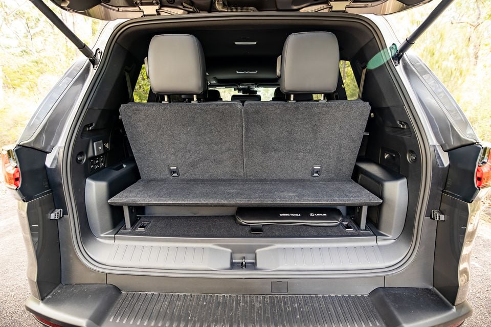 Boot interior of a Lexus LX700h Sport Luxury SUV with the third-row seats folded, showing under-floor storage with a warning triangle and a raised cargo floor panel, tailgate open