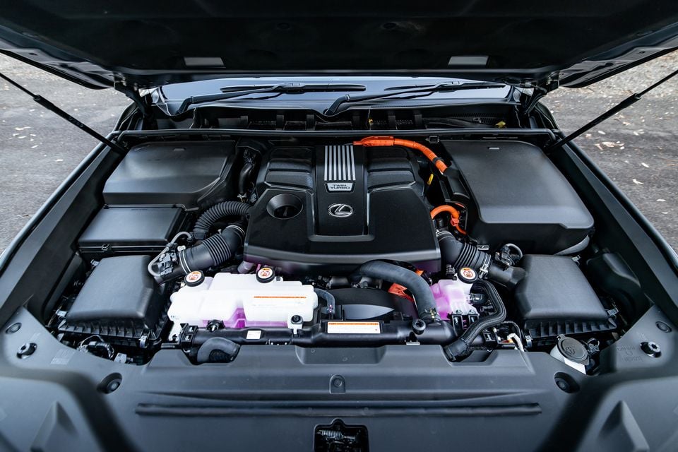 Lexus twin-turbo hybrid engine bay of a 2026 Lexus LX700h, showing the engine cover with orange high-voltage cables and fluid reservoirs with pink coolant