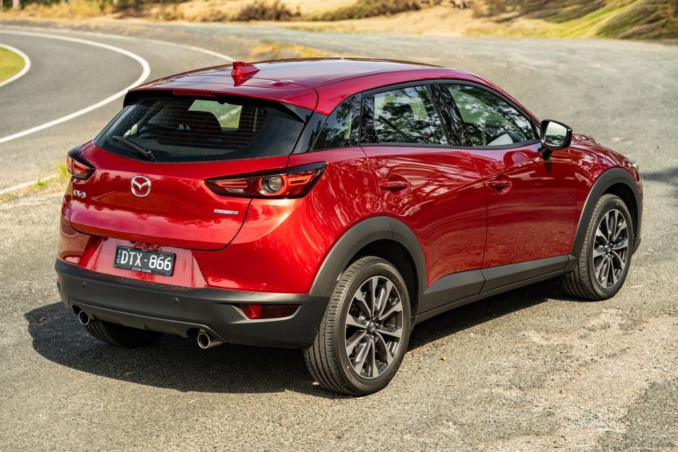 A red Mazda CX-3 small SUV seen from the rear three-quarter angle on a road
