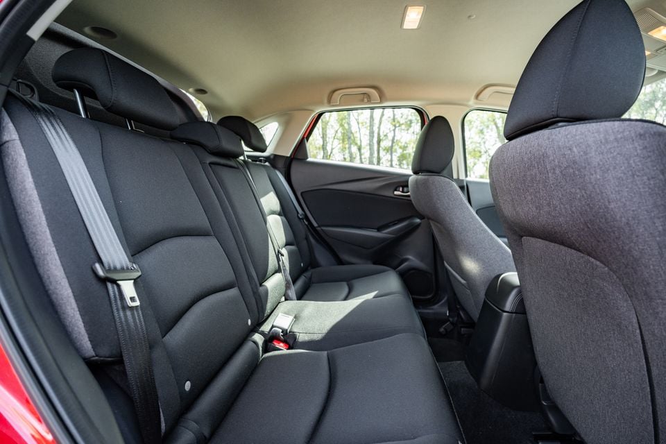 Rear passenger seats of a 2026 Mazda CX-3, showing dark fabric upholstery and seatbelts with trees visible through the windows