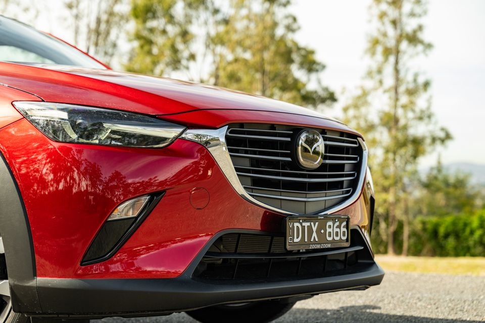 Close-up of the front grille and headlight of a red Mazda CX-3 SUV, showing the Mazda badge and front bumper detail