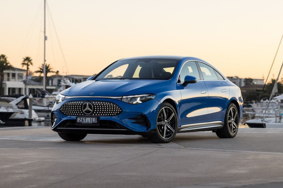 A blue 2026 Mercedes-Benz CLA 250 Electric sedan photographed from the front-side at a marina during sunset