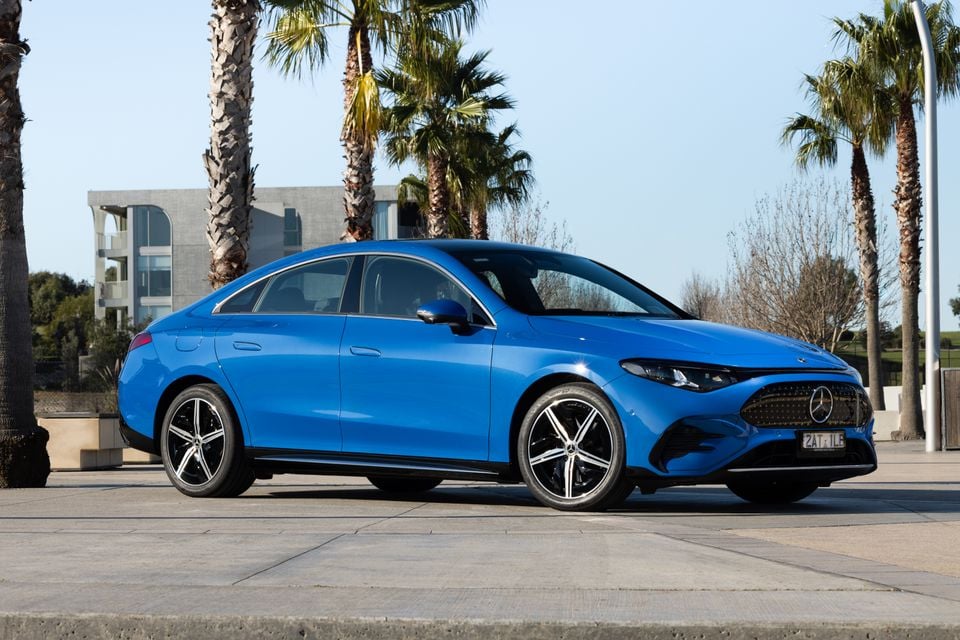 A blue 2026 Mercedes-Benz CLA sedan seen from the front-side, parked outdoors among palm trees with an Australian number plate visible.