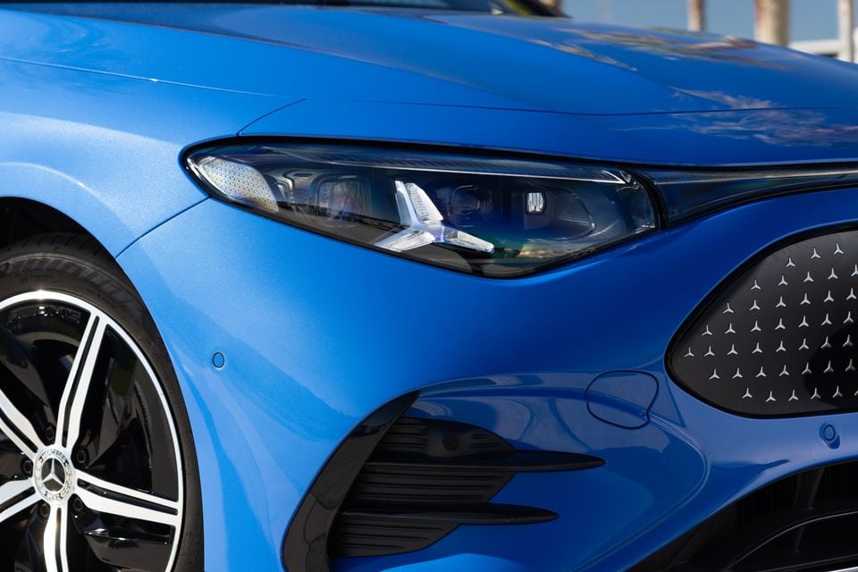 Close-up of the front headlight and grille on a blue Mercedes-Benz CLA electric, showing the star-pattern grille and LED headlight detail