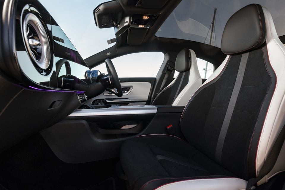 Interior of a 2026 Mercedes-Benz CLA 250 Electric showing the front seats with black and white upholstery with red contrast stitching, centre console, steering wheel, and ambient purple lighting