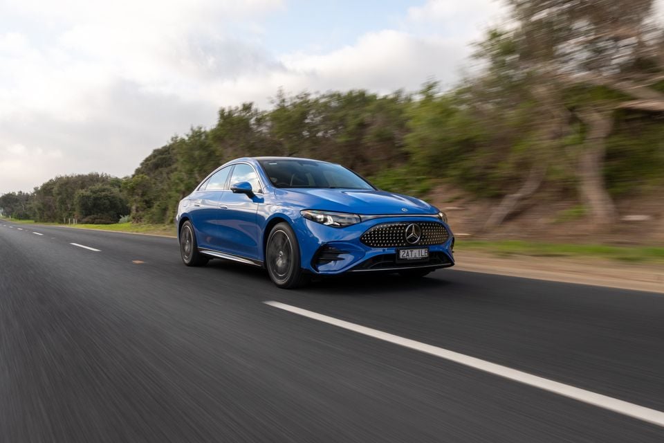 A blue 2026 Mercedes-Benz CLA 250 Electric sedan driving along an open road, seen from the front-side
