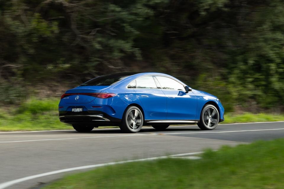 A blue Mercedes-Benz CLA electric sedan seen from the rear three-quarter angle while driving on a country road