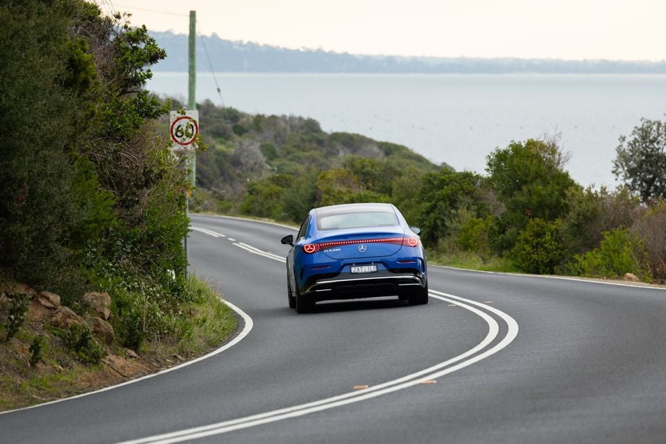 A blue Mercedes-Benz CLA 200 seen from the rear driving along a winding coastal road in Australia