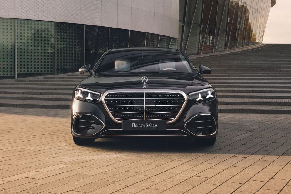 A black 2026 Mercedes-Benz S-Class sedan seen from the front, parked on a paved area outside a modern building.