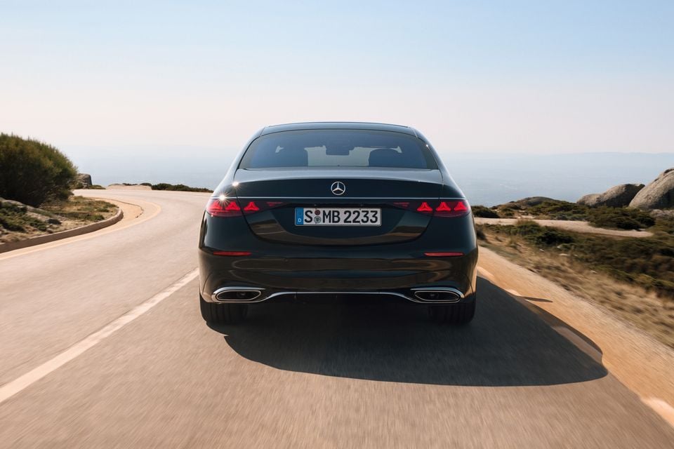 A dark green 2026 Mercedes-Benz S-Class sedan seen from the rear while driving along a coastal road