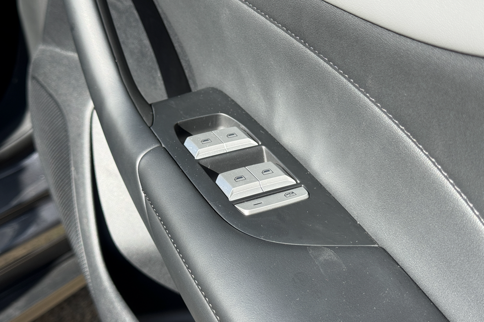 Power window controls on the door panel of a 2026 MG4 EV Essence, featuring chrome-finished buttons on a grey leather door trim.