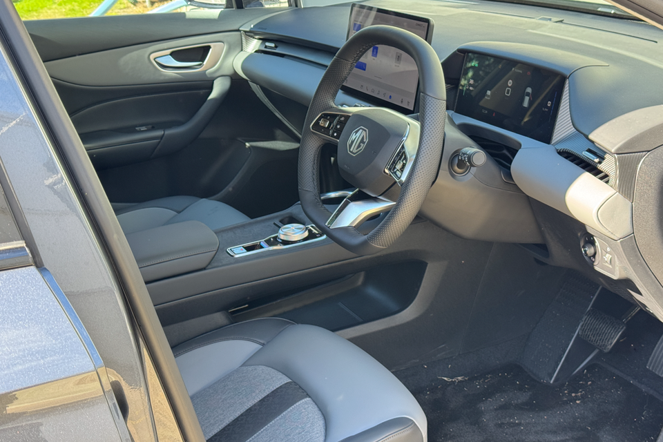 Interior of an MG4 EV showing the driver's seat, steering wheel with MG logo, dual screens on the dashboard, and centre console