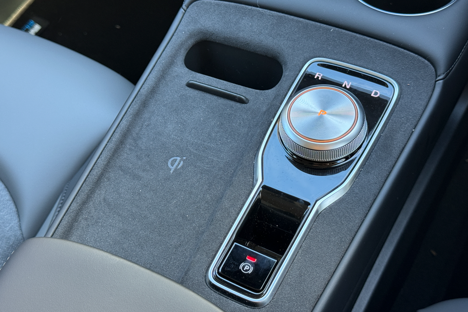 Close-up of the centre console in a 2026 MG4 EV Essence, showing a rotary gear selector dial with R, N and D positions, a park button, and a Qi wireless charging pad.