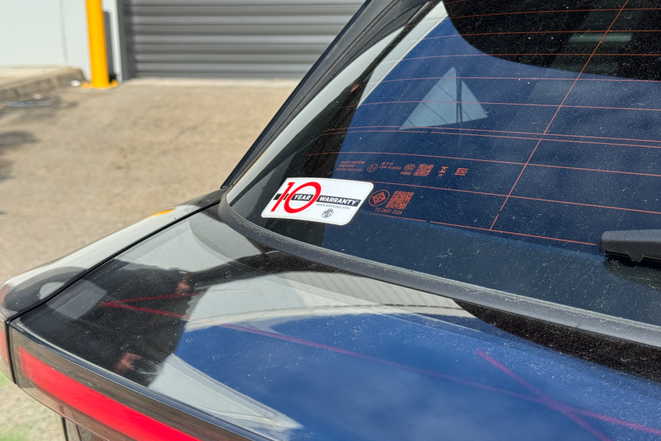 Close-up of the rear window of a blue MG 4 EV showing a 10-year warranty sticker on the glass