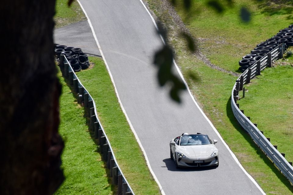 A silver 2026 MG Cyberster convertible driving on a winding race track lined with tyre barriers and guard rails, seen from above