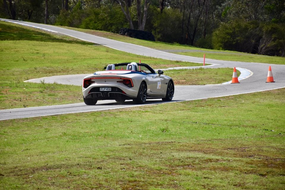 A white 2026 MG Cyberster convertible with its roof down driving on a race track, seen from the rear