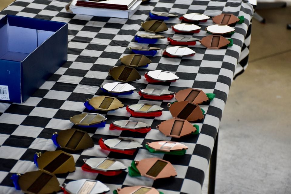 Rows of gold, silver and bronze medals with blue, red and green ribbons laid out on a black and white chequered tablecloth