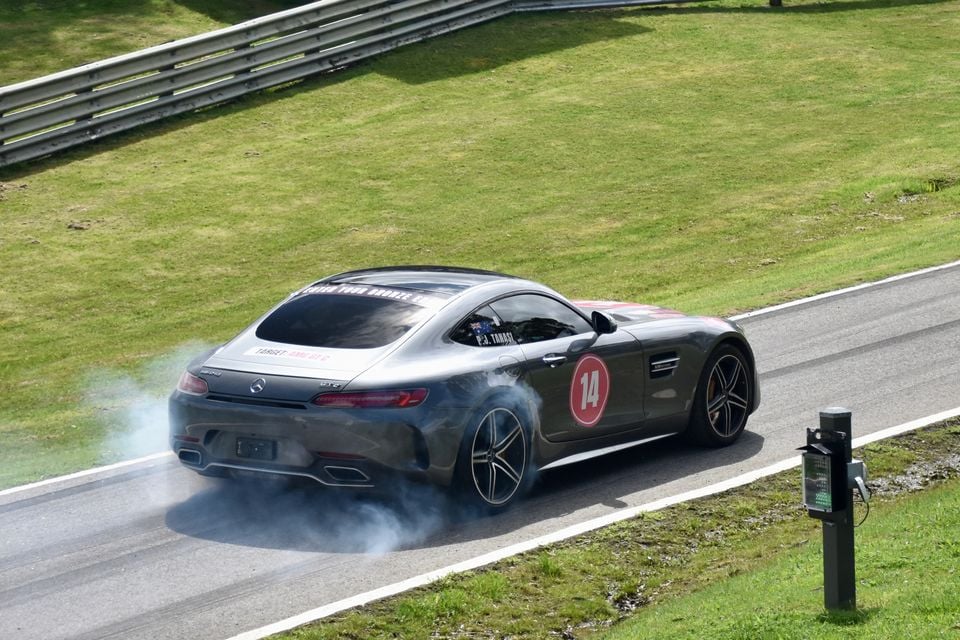 A grey Mercedes-AMG GT C coupe with race number 14 spinning its rear tyres in a cloud of smoke on a racetrack, seen from the rear