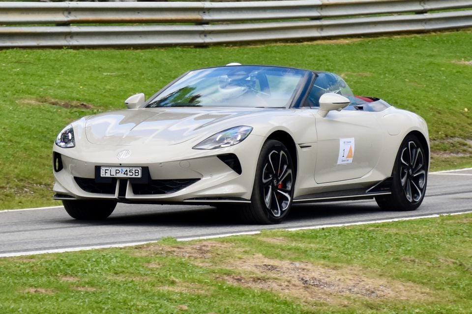 A cream 2026 MG Cyberster convertible sports car with its roof down, driving on a race track lined with grass and a guardrail