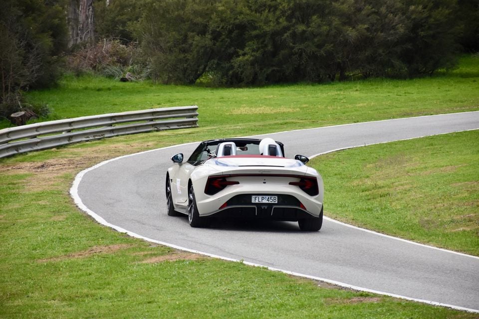 A white 2026 MG Cyberster convertible with its roof down, seen from the rear while driving through a bend on a race circuit