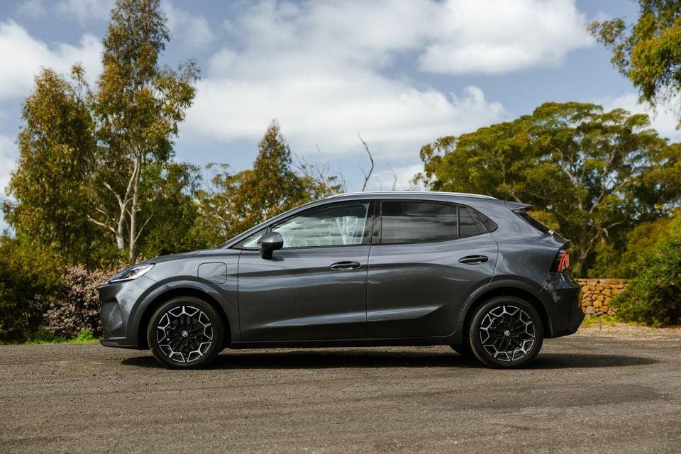 A grey MG4 Urban EV hatchback seen from the side, parked on a gravel surface with Australian bush in the background
