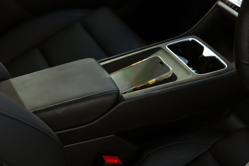 A smartphone resting on the centre console wireless charging pad of a 2026 MG4 Urban EV, with the leather armrest and cup holders visible nearby.