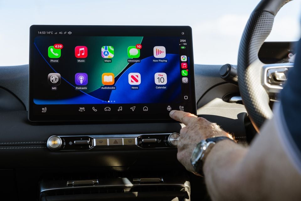 A person touching the touchscreen infotainment display in an MG4, showing Apple CarPlay with apps including Phone, Music, Maps and Messages