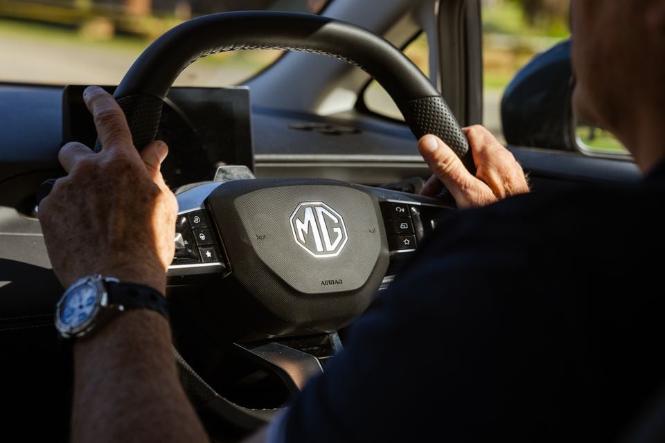 A driver's hands on the MG-branded steering wheel inside a 2026 MG4 Urban EV, showing the airbag hub and steering wheel controls