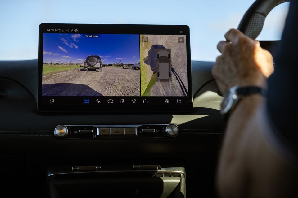 A car's touchscreen infotainment display showing a 360-degree camera system with front view and bird's-eye view, as seen from the driver's seat