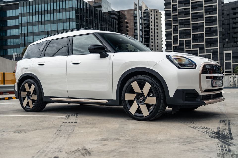 A white Mini Countryman SUV parked on a rooftop car park with city buildings in the background, seen from the front-side angle