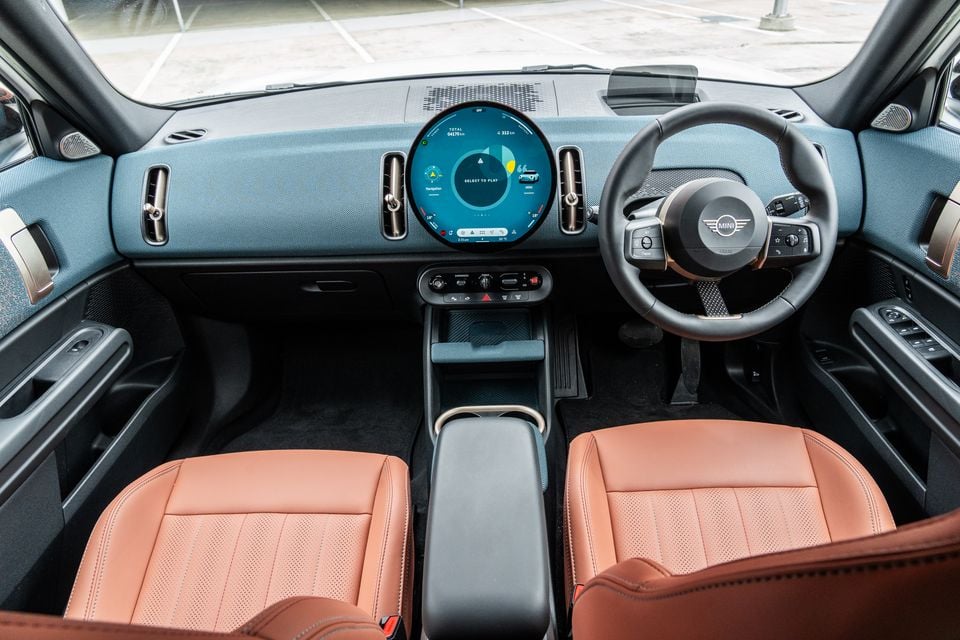 Interior of a MINI Countryman SE Favoured showing the round circular infotainment touchscreen, blue dashboard, tan leather seats, and right-hand-drive steering wheel with MINI logo