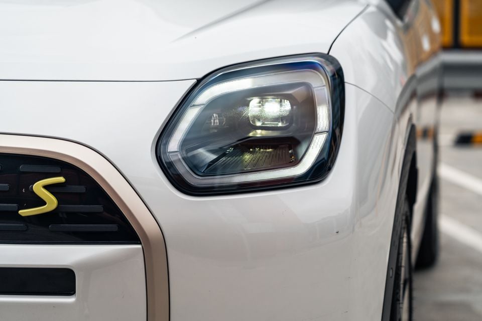 Close-up of the LED headlight on a white Mini Countryman S, showing the daytime running light detail and gold S badge on the grille.