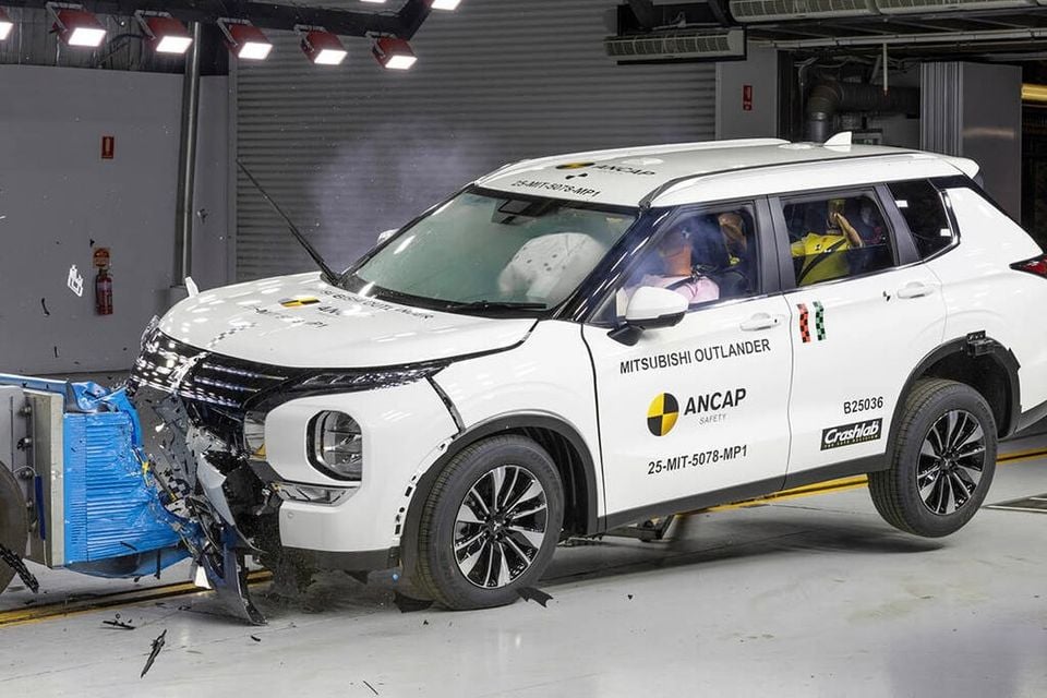 A white Mitsubishi Outlander SUV undergoing an ANCAP frontal crash test, with front-end damage and airbags deployed