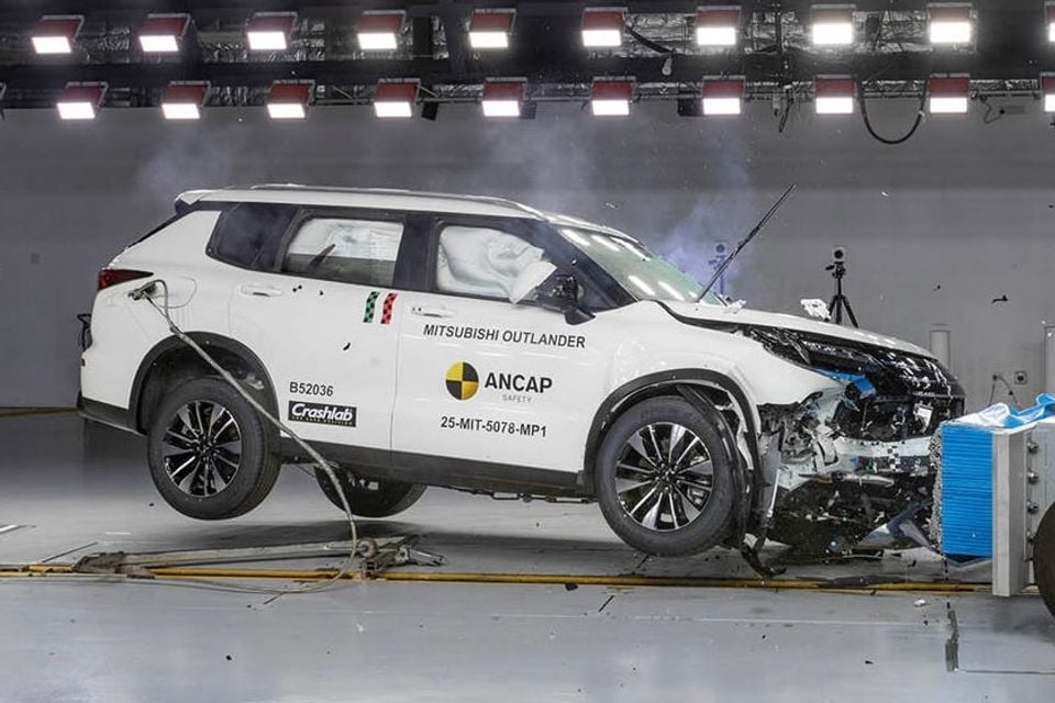 A white Mitsubishi Outlander SUV undergoing an ANCAP frontal crash test, with severe front-end damage and airbags deployed