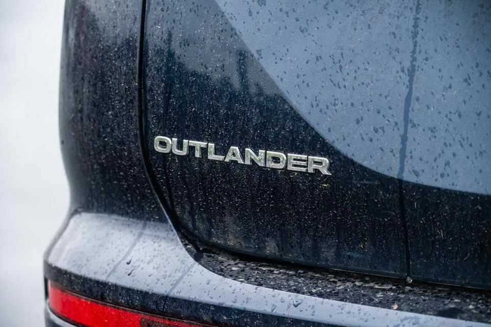 Close-up of the 'Outlander' badge on the rear of a mud-speckled Mitsubishi Outlander SUV