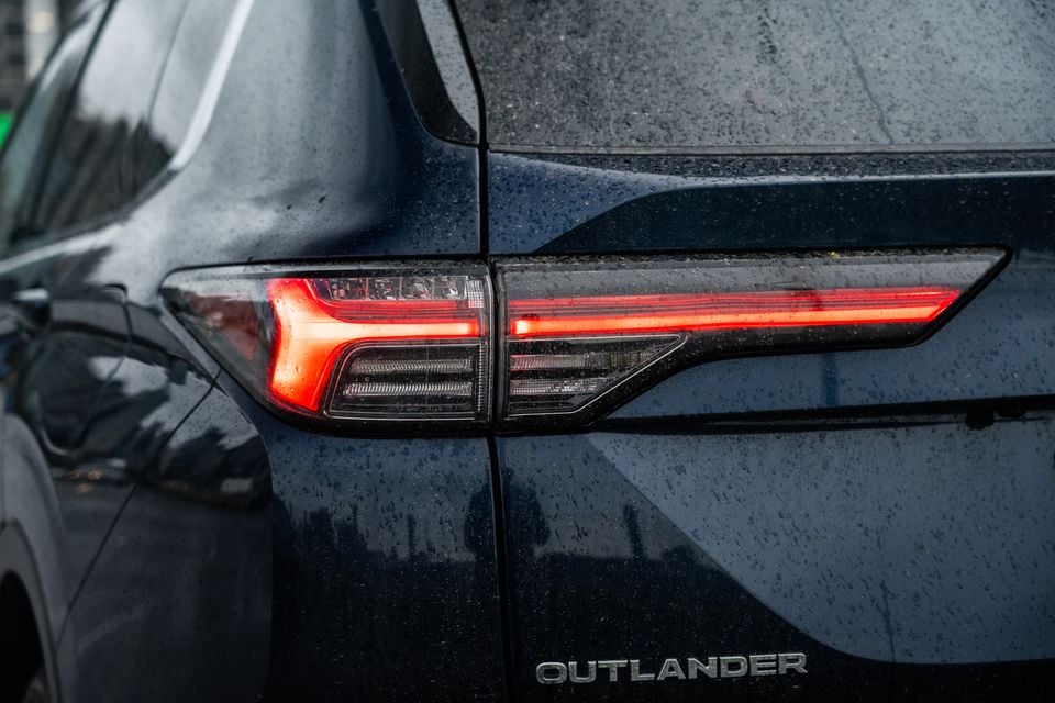 Close-up of the rear tail light and Outlander badge on a dark blue Mitsubishi Outlander, wet with rain