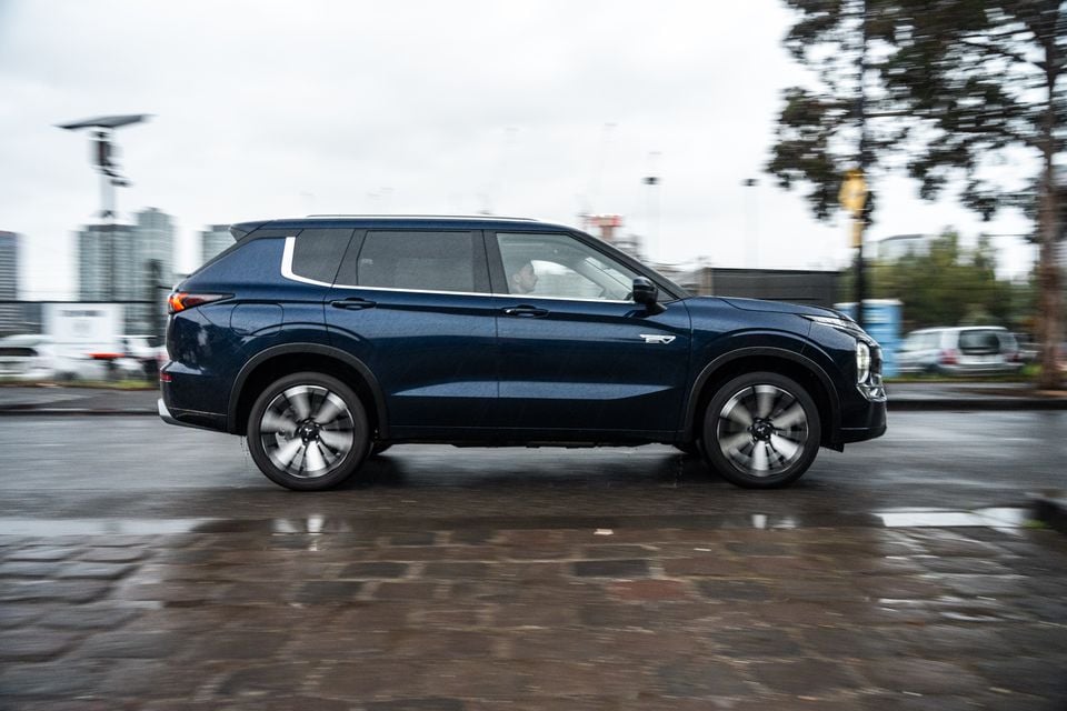 A dark blue 2026 Mitsubishi Outlander PHEV SUV seen from the side while driving on a wet urban street