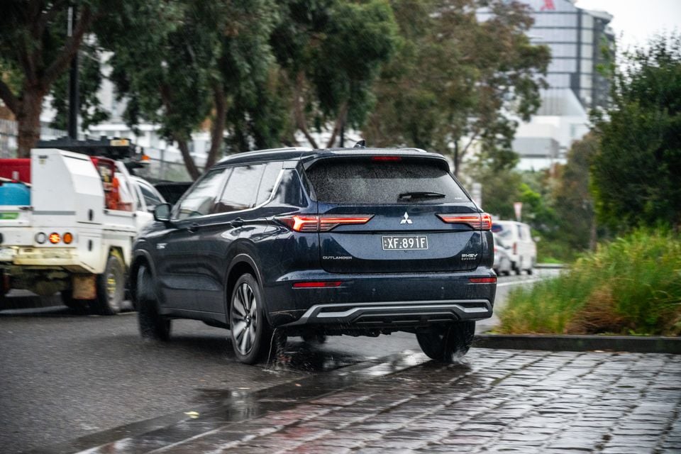 A dark blue Mitsubishi Outlander PHEV Exceed SUV seen from the rear while driving on wet city streets in Australia