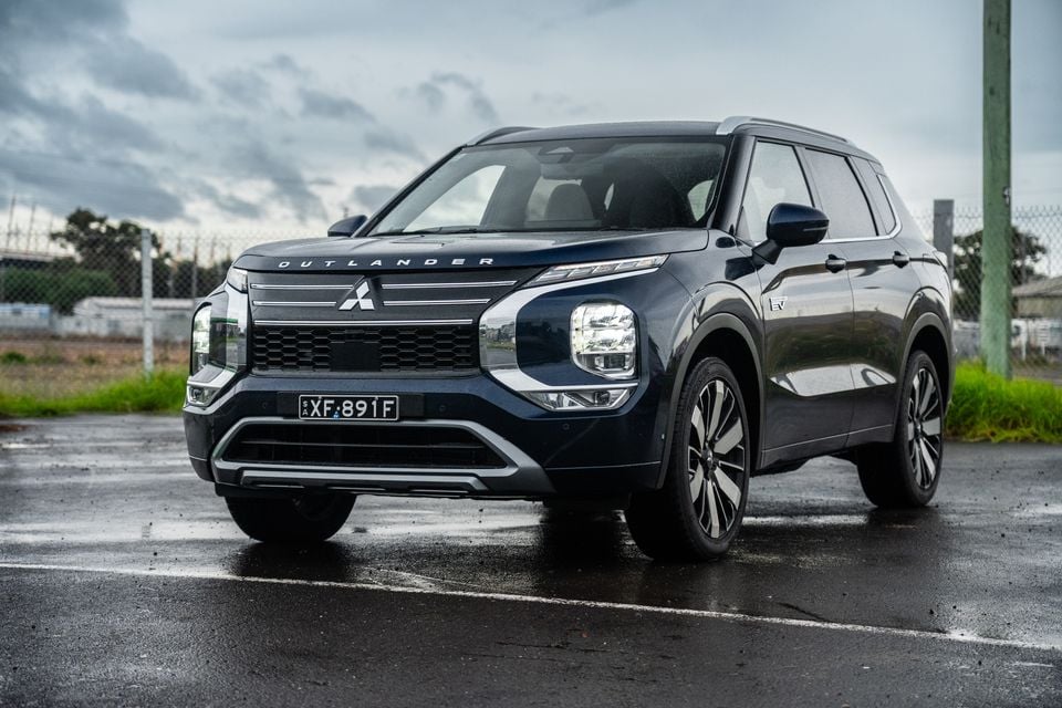 A dark blue 2026 Mitsubishi Outlander PHEV SUV seen from the front-side angle on a wet road