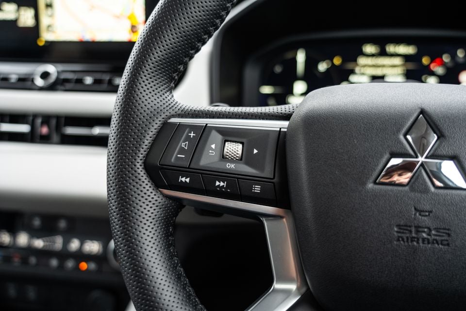 Close-up of the Mitsubishi Outlander steering wheel showing audio and media controls, with the Mitsubishi logo and SRS airbag badge visible