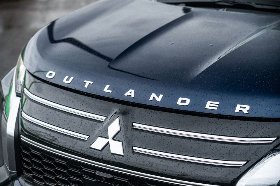 Close-up of the Mitsubishi Outlander front grille and bonnet badge with chrome detailing and the Outlander name badge, wet with rain