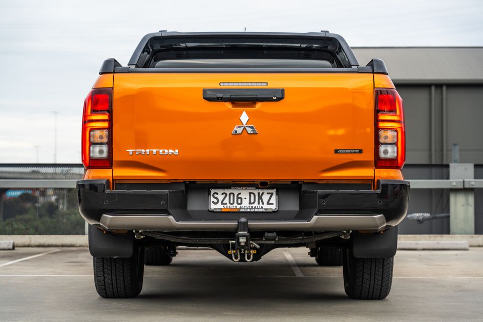 An orange 2026 Mitsubishi Triton GSR dual-cab ute seen from the rear, parked on a rooftop car park with a tow bar fitted