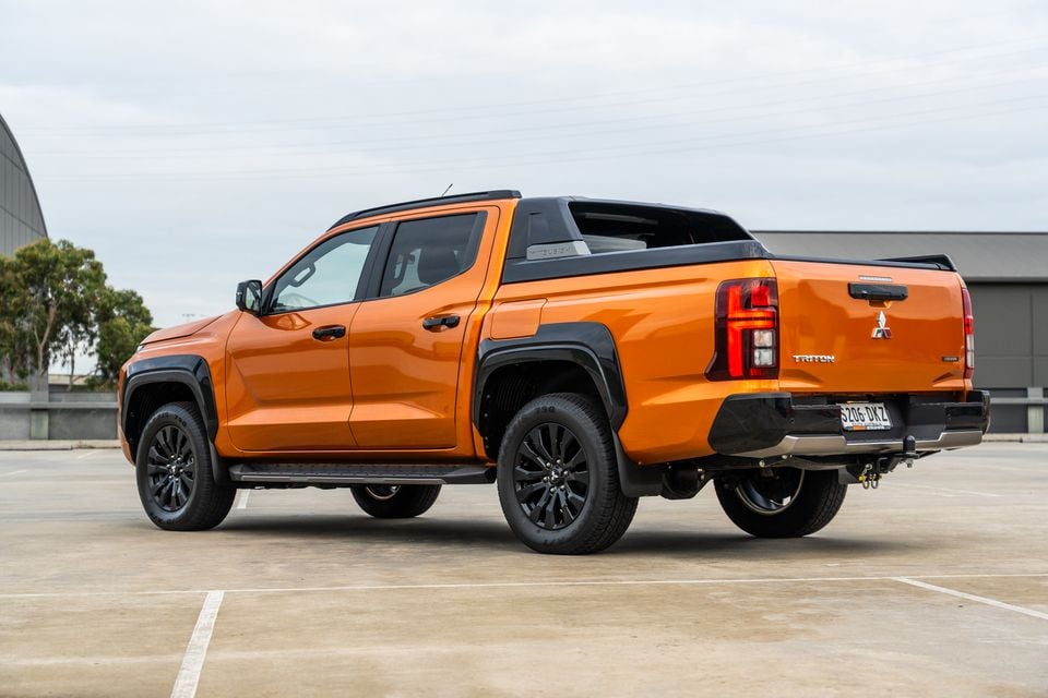 An orange 2026 Mitsubishi Triton GSR dual-cab ute with black wheels and sports bar, seen from the rear quarter, parked on a rooftop car park