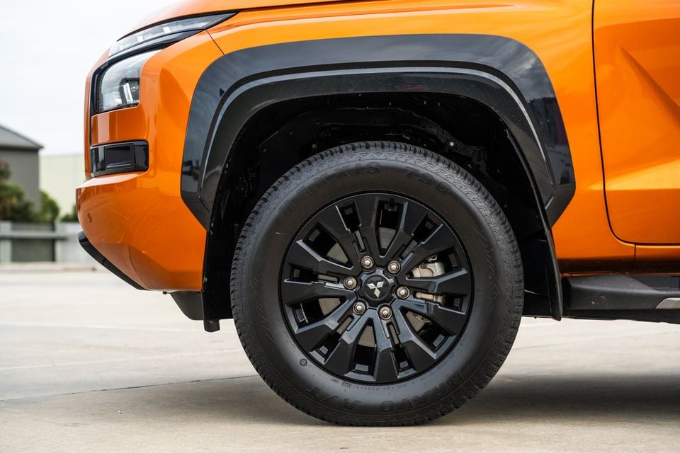 Close-up of the black alloy wheel and flared front guard on an orange 2026 Mitsubishi Triton GSR ute