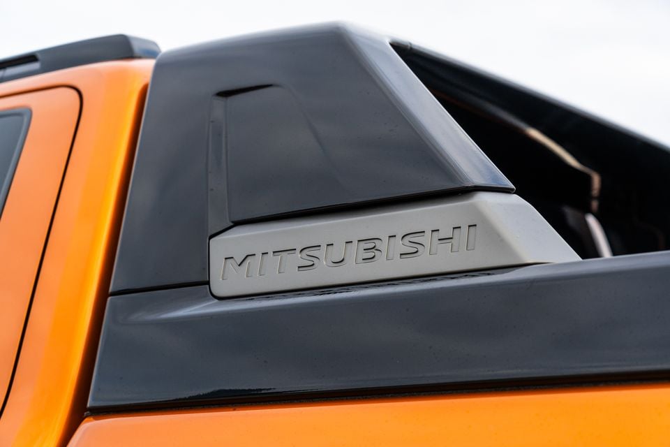Close-up of the black sports bar with embossed Mitsubishi lettering on an orange 2026 Mitsubishi Triton GSR ute, behind the rear door