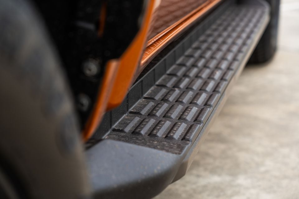 Close-up of the black side step on an orange 2026 Mitsubishi Triton GSR ute, with orange body trim above and a tyre in the foreground