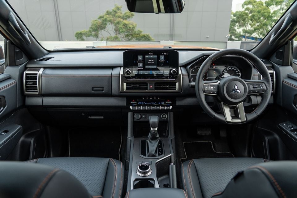 Dashboard of the 2026 Mitsubishi Triton GSR with touchscreen, digital instruments, steering wheel and black leather seats with orange stitching